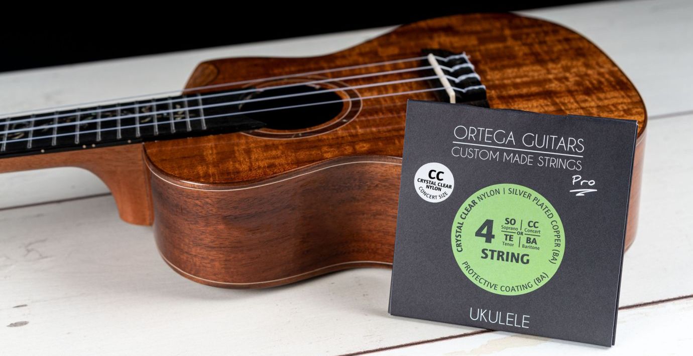 Eine Packung Saiten steht vor einer Ukulele von Ortega